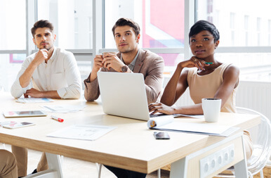 Three colleagues in a meeting around a table with a laptop