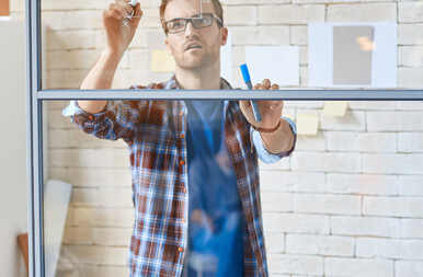 A colleague sketching ideas on a glass wall with sticky notes